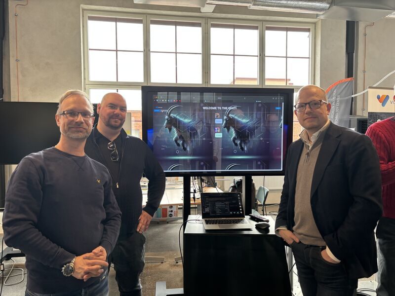 Three people at the project stand with the assistant running on a screen